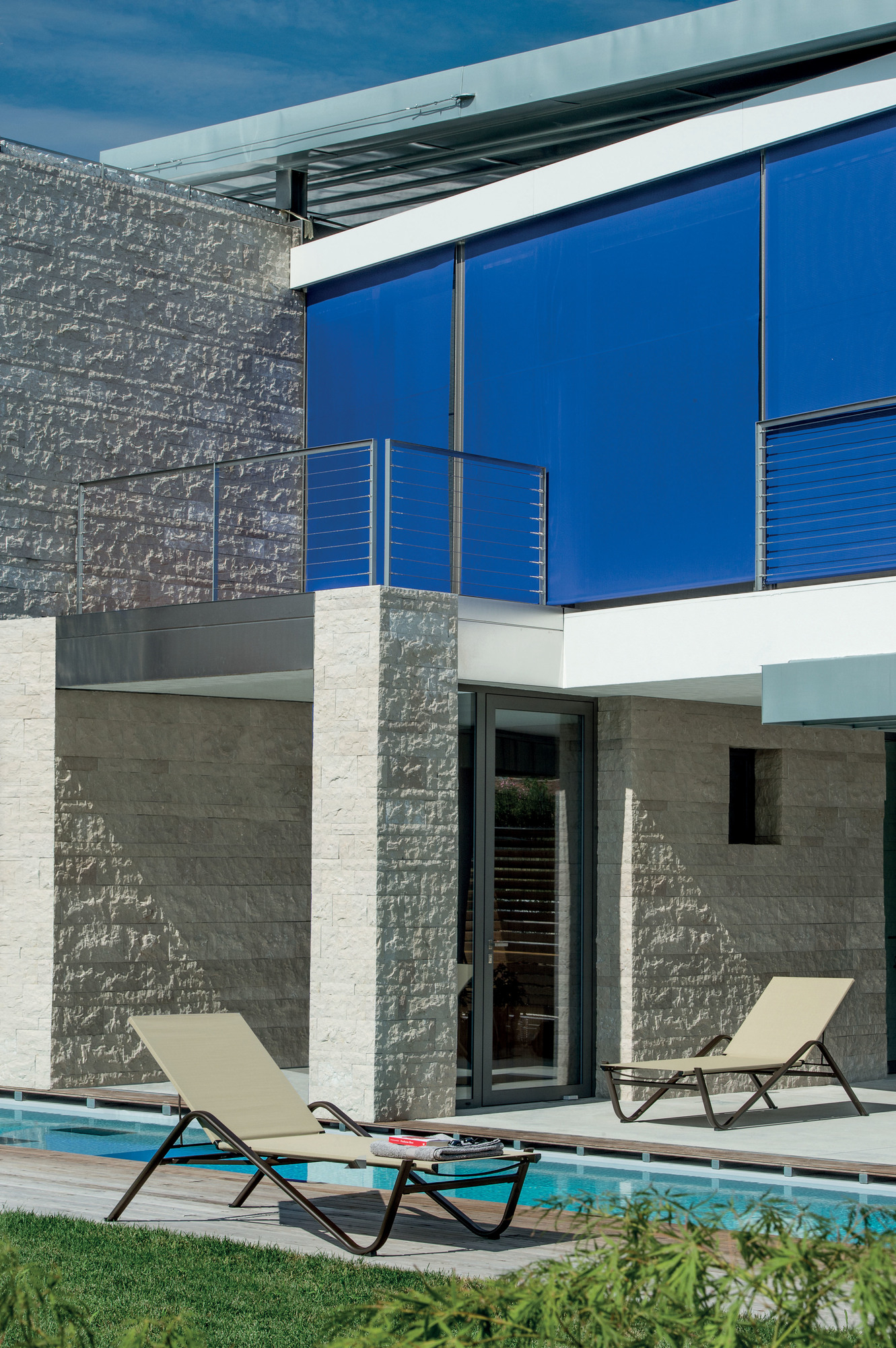 Zwei Emu Holly Sonnenliegen in Beige am Pool eines modernen Hauses.