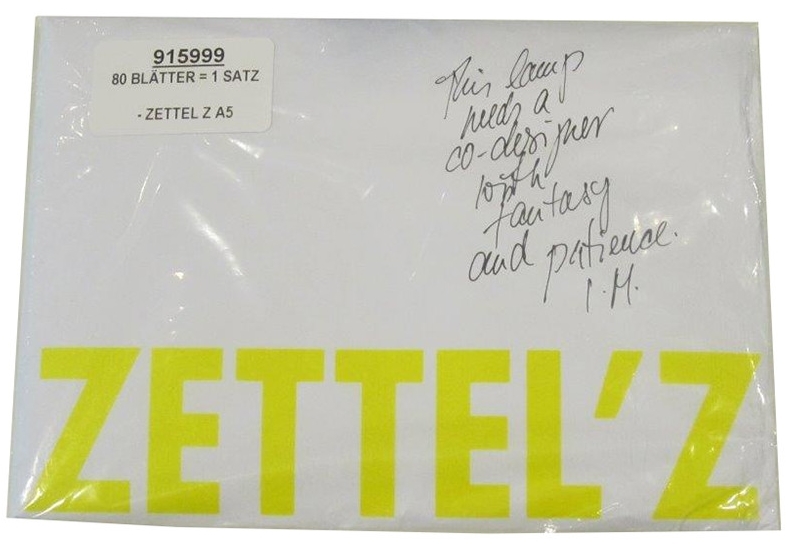 Verpackter Zettelsatz A5 für Ingo Maurer Zettel'z Leuchte mit gelbem Schriftzug und handschriftlichem Zitat.