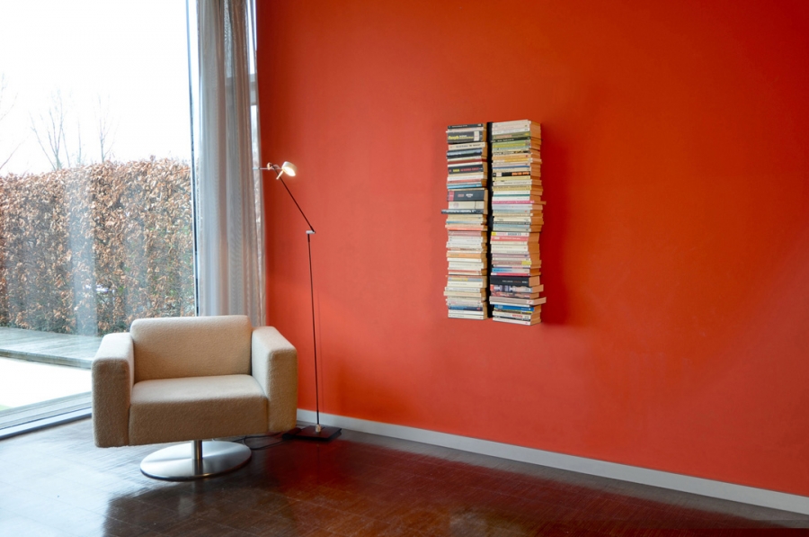 Booksbaum Wandregal in Schwarz an roter Wand mit Büchern, neben Sessel und Lampe.