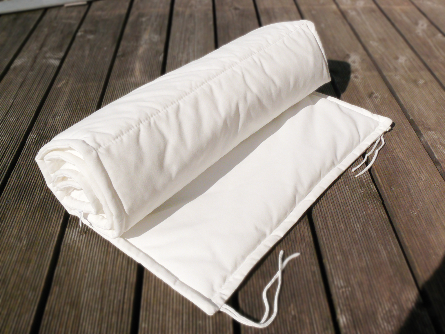 Weiße, gerollte Jan Kurtz Luxury Auflage für Gartenmöbel auf Holzterrasse. Bequeme Polsterauflage.