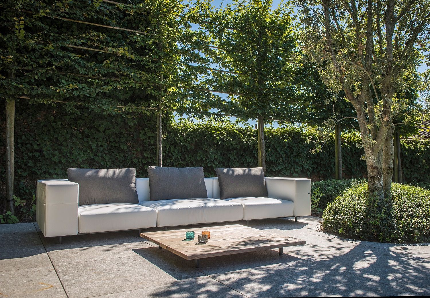 Walrus Outdoor Sofa von Extremis, weißes Eckmodul mit grauen Kissen im Garten.