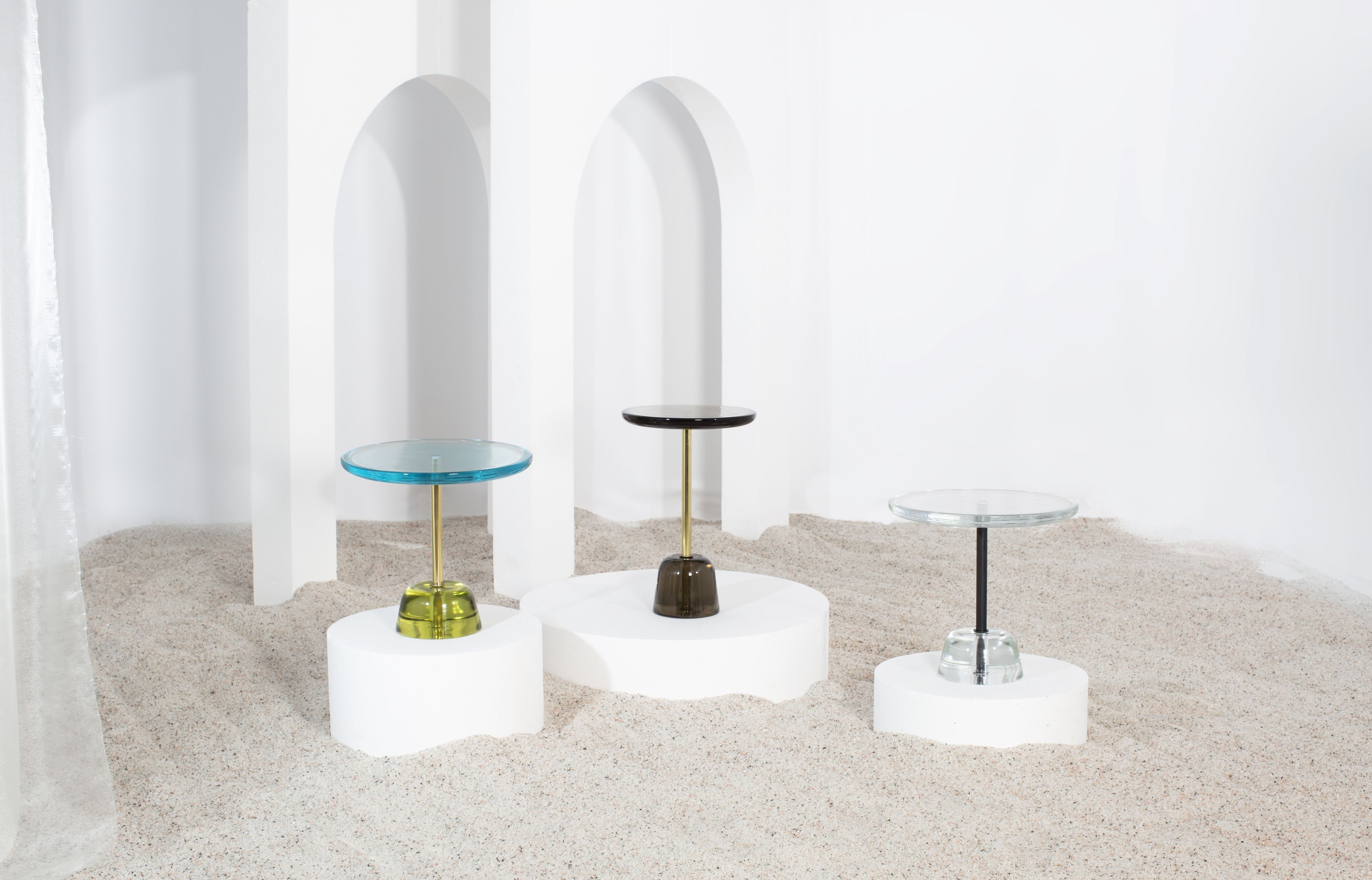 Drei moderne Beistelltische von Pulpo mit Glasplatte und farbigen Sockeln auf Sand.