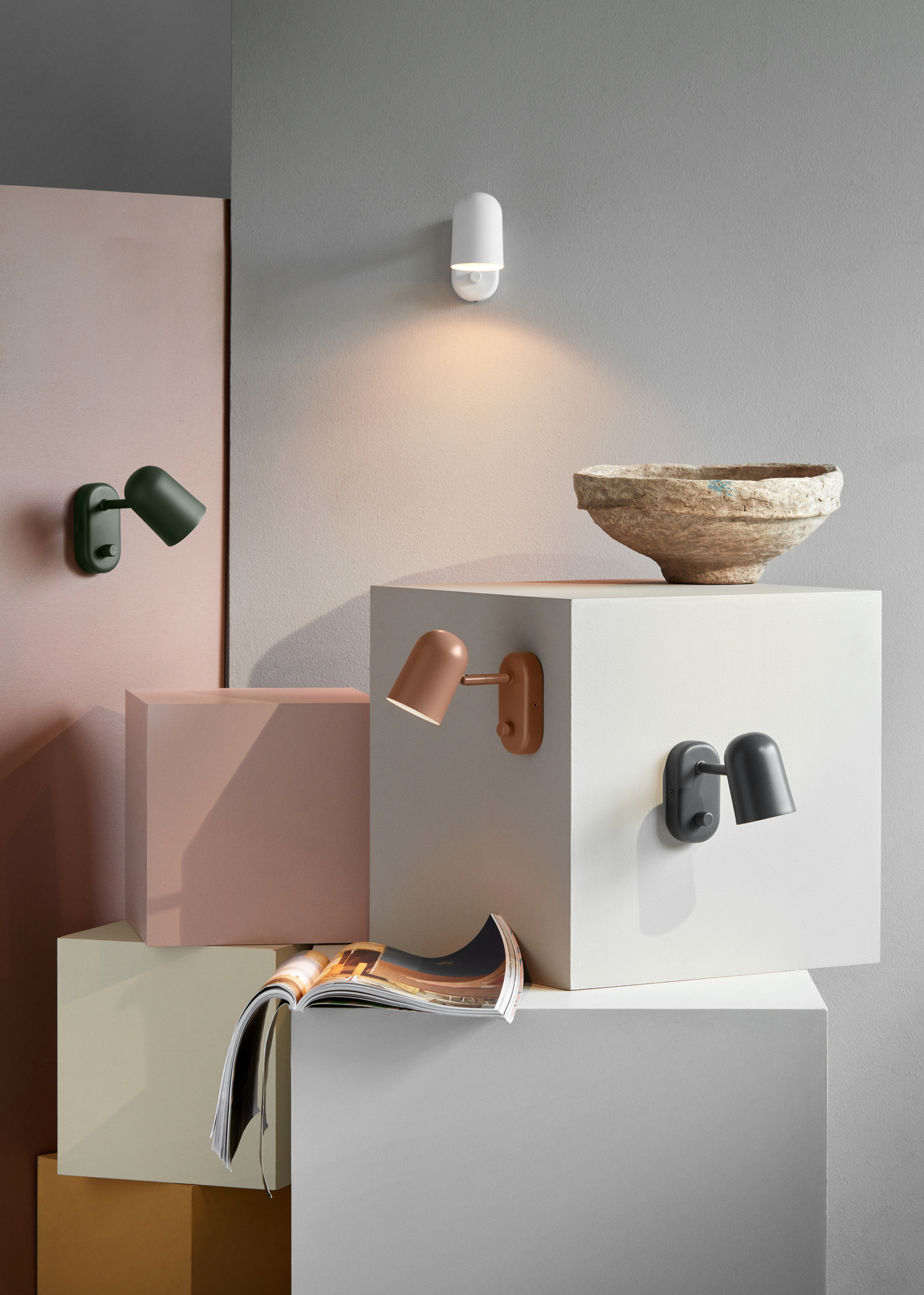 Mehrere Buddy Wandleuchten von Northern in verschiedenen Farben auf gestapelten Blöcken.