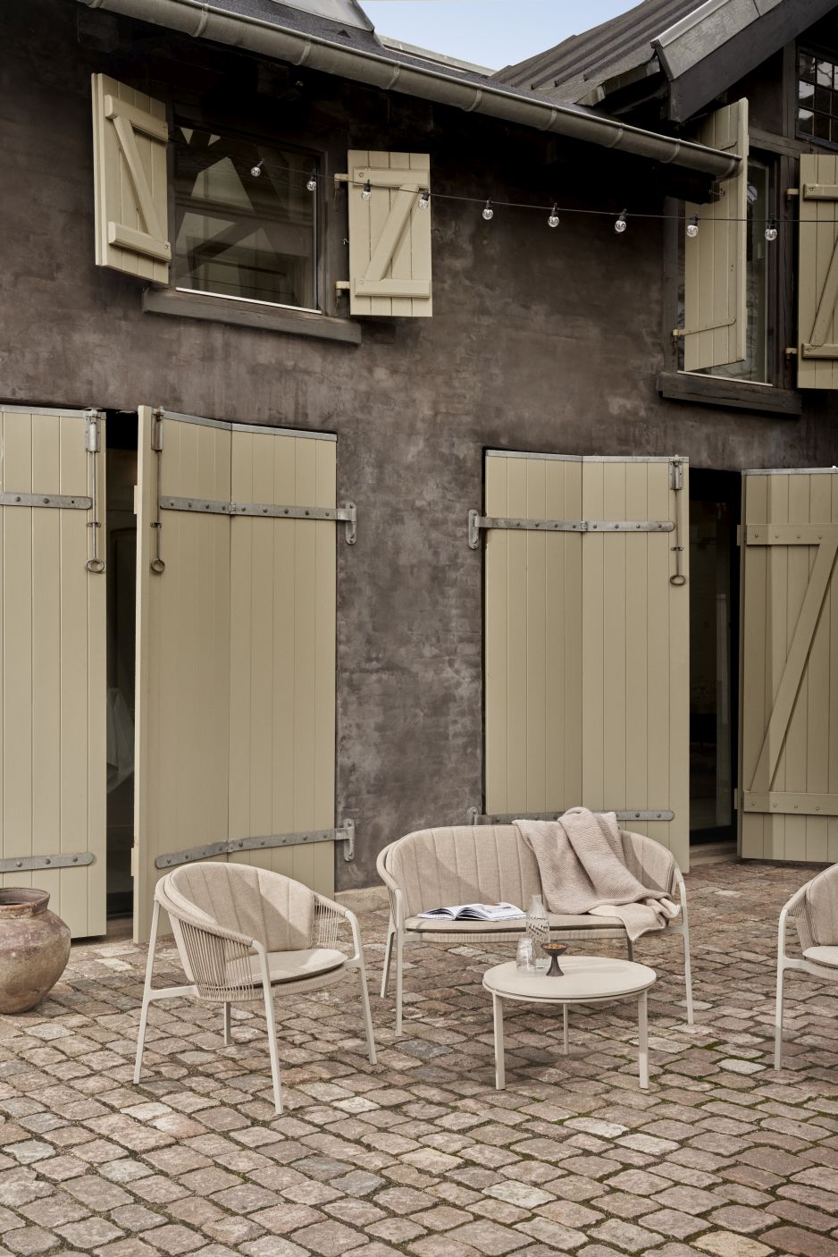 Lagrasse Zweisitzer Sofa von Vipp mit Outdoor-Möbeln und Beistelltisch auf gepflastertem Innenhof.