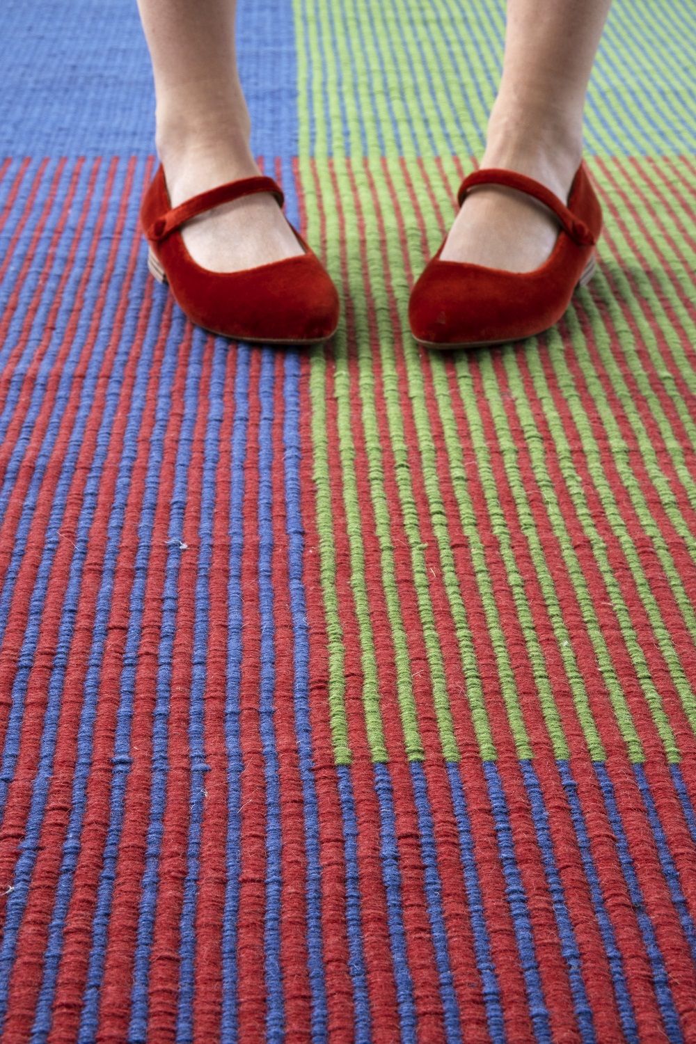 Detailaufnahme: Füße mit roten Schuhen auf dem gestreiften Haze Runner Teppich von Nanimarquina.