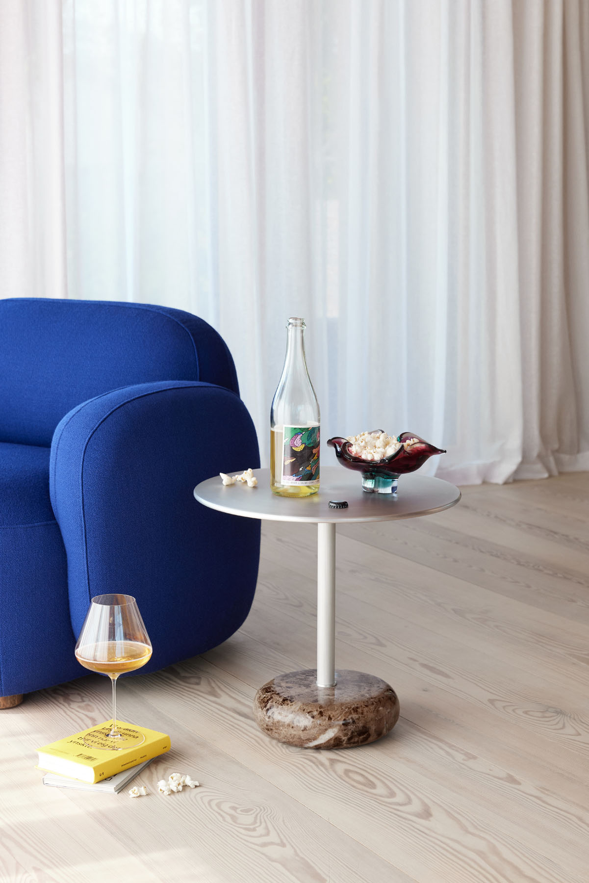 Northern Ton Beistelltisch H50cm neben blauem Sessel, mit Getränk, Popcorn und Buch auf hellem Holzboden.