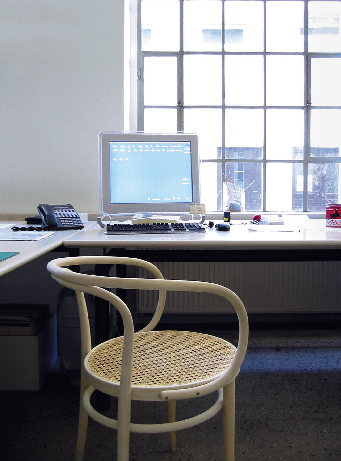 Detailaufnahme: Weißer 209 Bugholz Stuhl von Thonet mit Wiener Geflecht vor Schreibtisch.