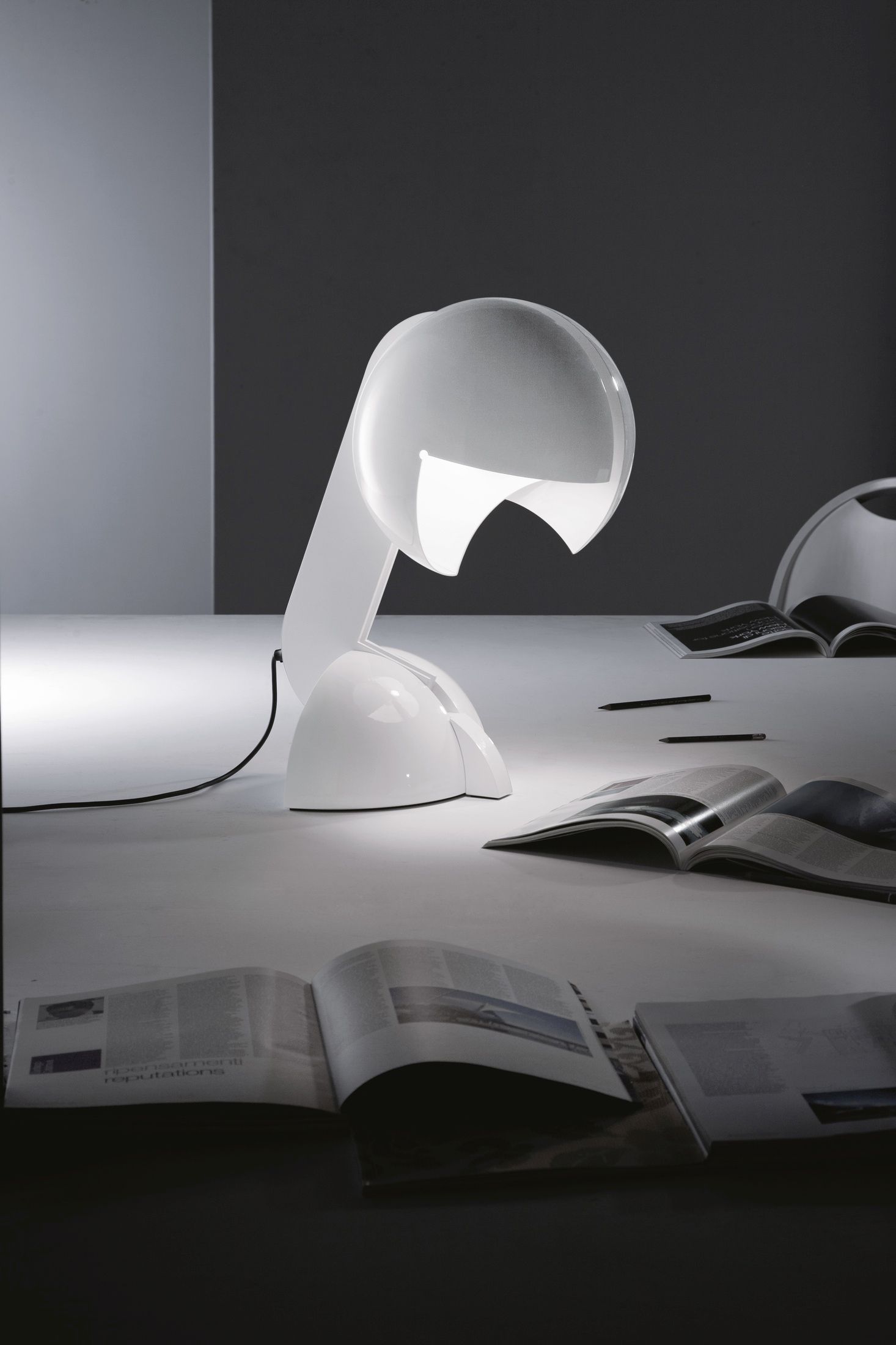 Weiße Ruspa Tischleuchte von Martinelli Luce auf einem Tisch mit Magazinen und Stiften.