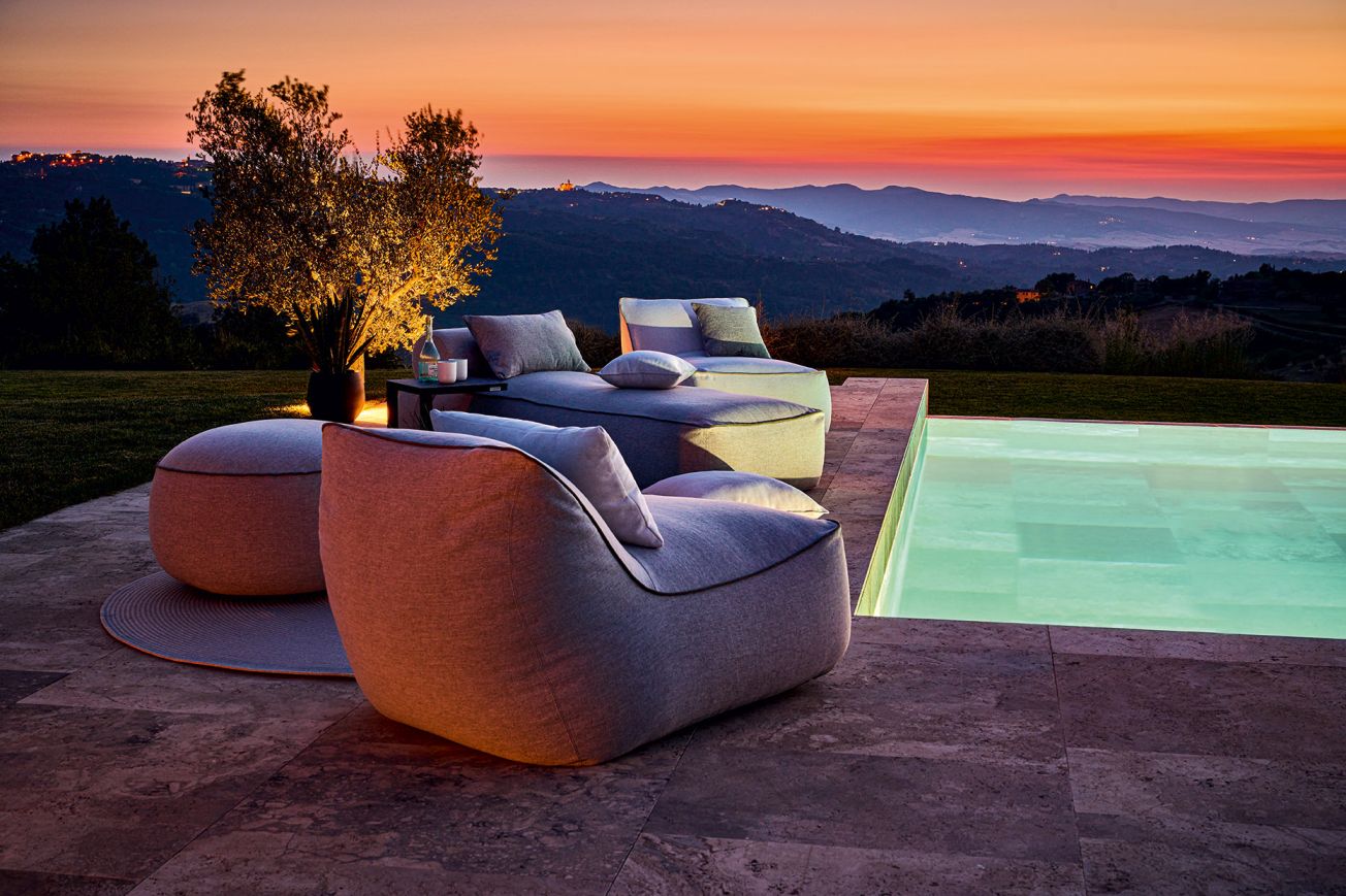 Maliha Lounge Hocker von Weishäupl, runder Outdoor Sitzhocker in Grau, Poollandschaft bei Sonnenuntergang.