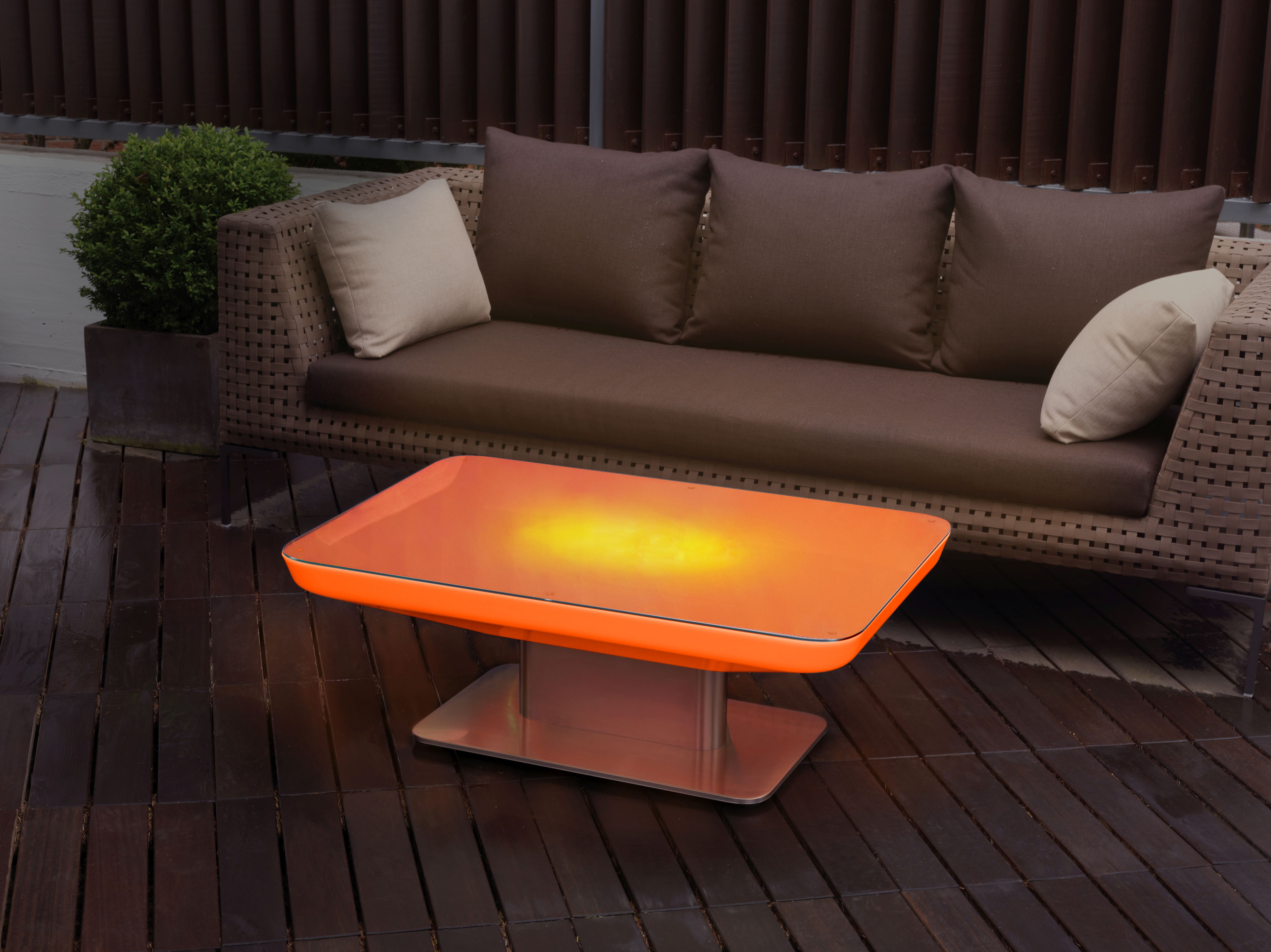 Studio 45 LED Tisch von Moree, orangefarben, beleuchtet, neben einer braunen Outdoor-Couch auf Holzterrasse.