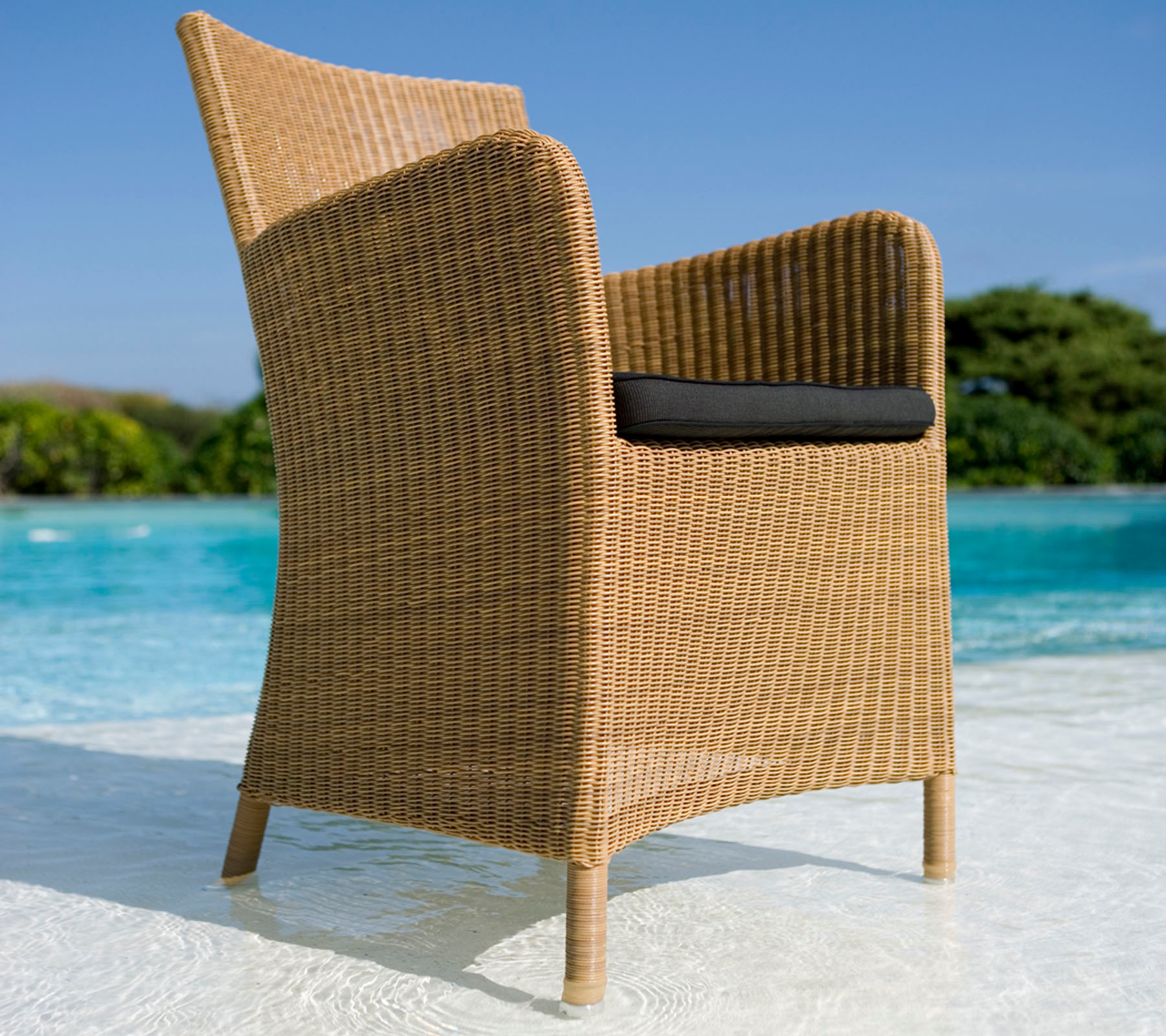 Heller Rattansessel mit dunklem Sitzkissen, Teil der Cane-Line Hampsted Gartenmöbel Kollektion.