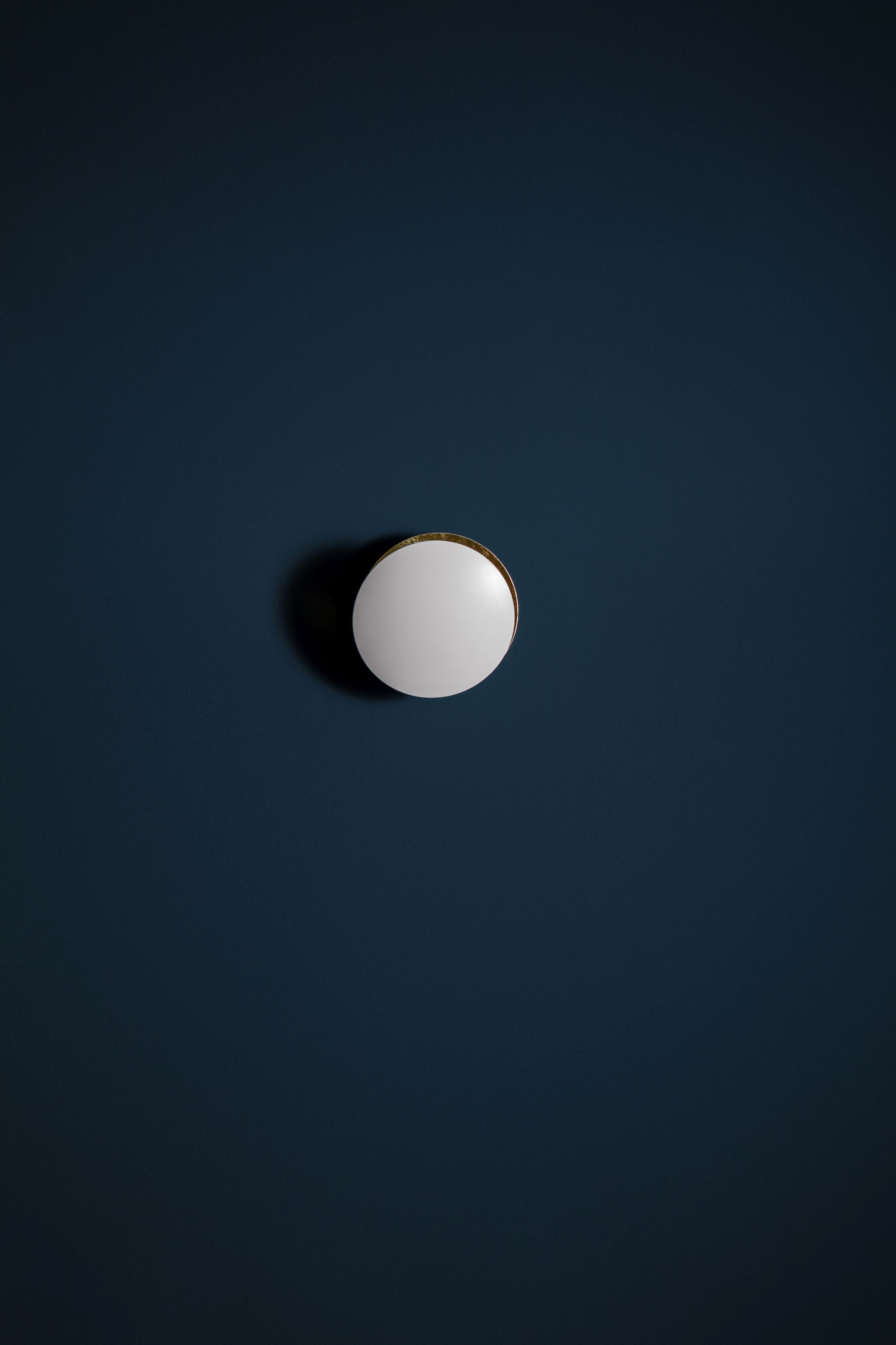 Weiße Lederam Wandleuchte von Catellani & Smith an dunkelblauer Wand. Design Lampe für Wohnzimmer.