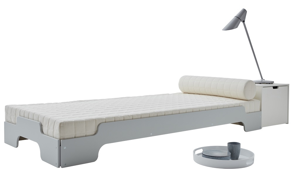 Graue Stapelliege Klassik von Müller Möbelwerkstätten mit Matratze, Kissenrolle, Nachttisch und Lampe.