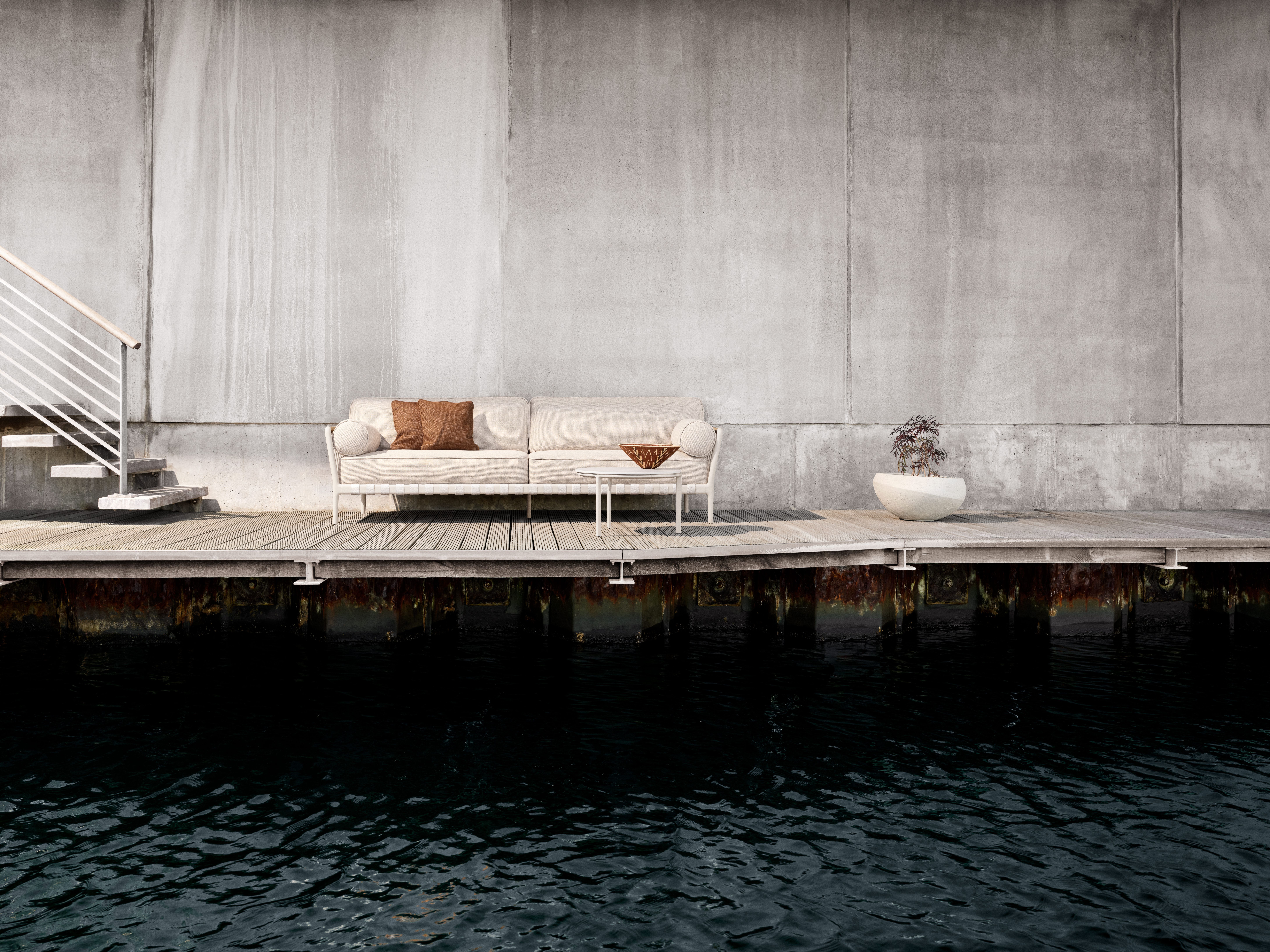 Open-Air Outdoor Vipp Kaffeetisch Ø60 mit Sofa und Pflanze auf Holzterrasse am Wasser.