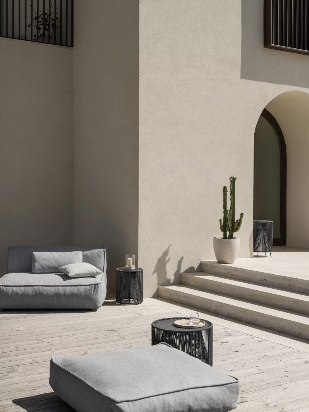 Graues Outdoor-Sofa mit Blomus Grow Kissen 38x38 cm und Beistelltischen auf einer Terrasse.