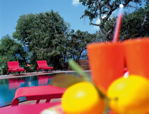Zwei rote Fermob Dune Sonnenliegen am Pool mit Getränken und Zitronen im Vordergrund.