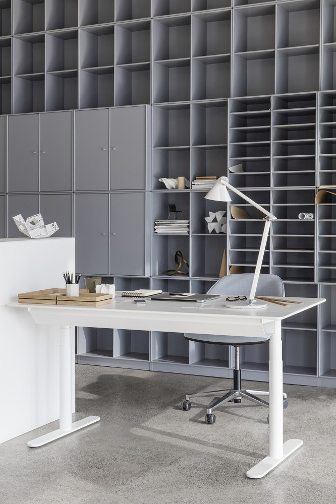 Weißer HiLow Arbeitstisch mit Schiebeplatte von Montana, höhenverstellbar, im modernen Büro mit Regalen.