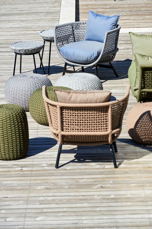 Outdoor-Szene mit Suka Lounge Sessel von Jan Kurtz, Poufs und Beistelltischen auf einer Holzterrasse.