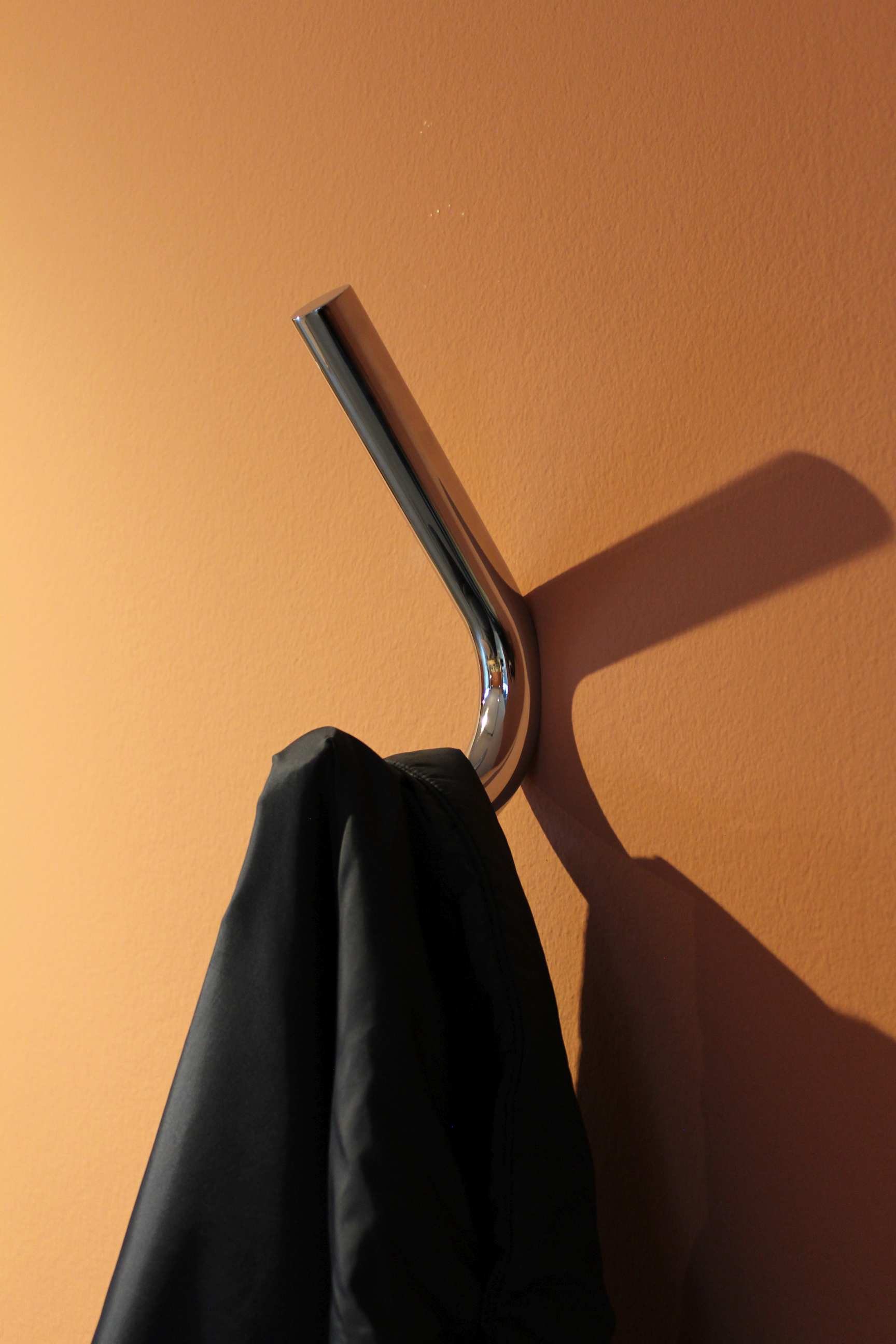 Nahaufnahme des S 12 Wandhaken von Thonet mit einer schwarzen Jacke an einer orangefarbenen Wand.