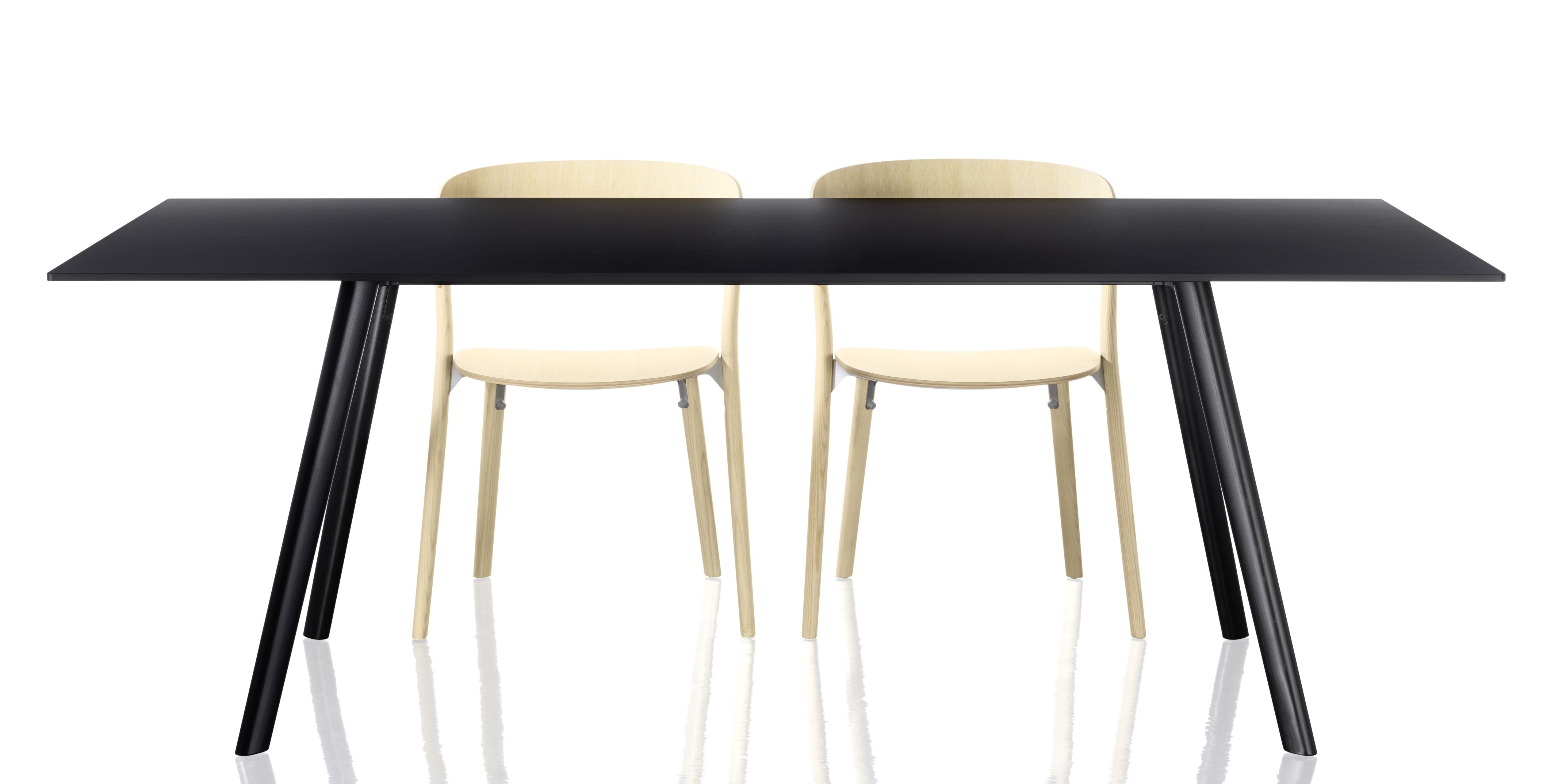 Zwei helle Holzstühle vom Typ Pila Stuhl stehen an einem schwarzen Esstisch.