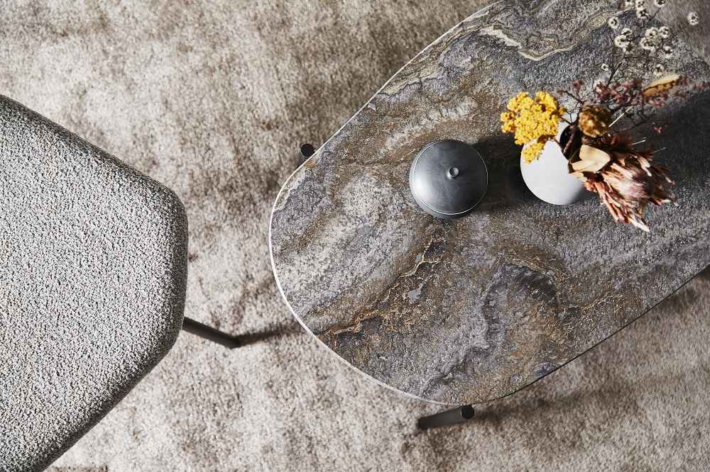 Grau melierter La Terra Couchtisch von Woud mit Blumen und Dose auf einem Teppich.