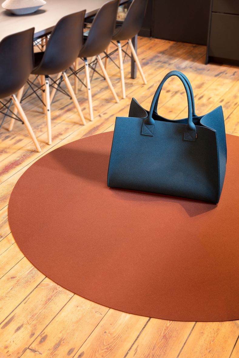 Runder, terracottafarbener Hey Sign Teppich Bigdot aus Filz auf Holzboden mit blauer Filztasche.
