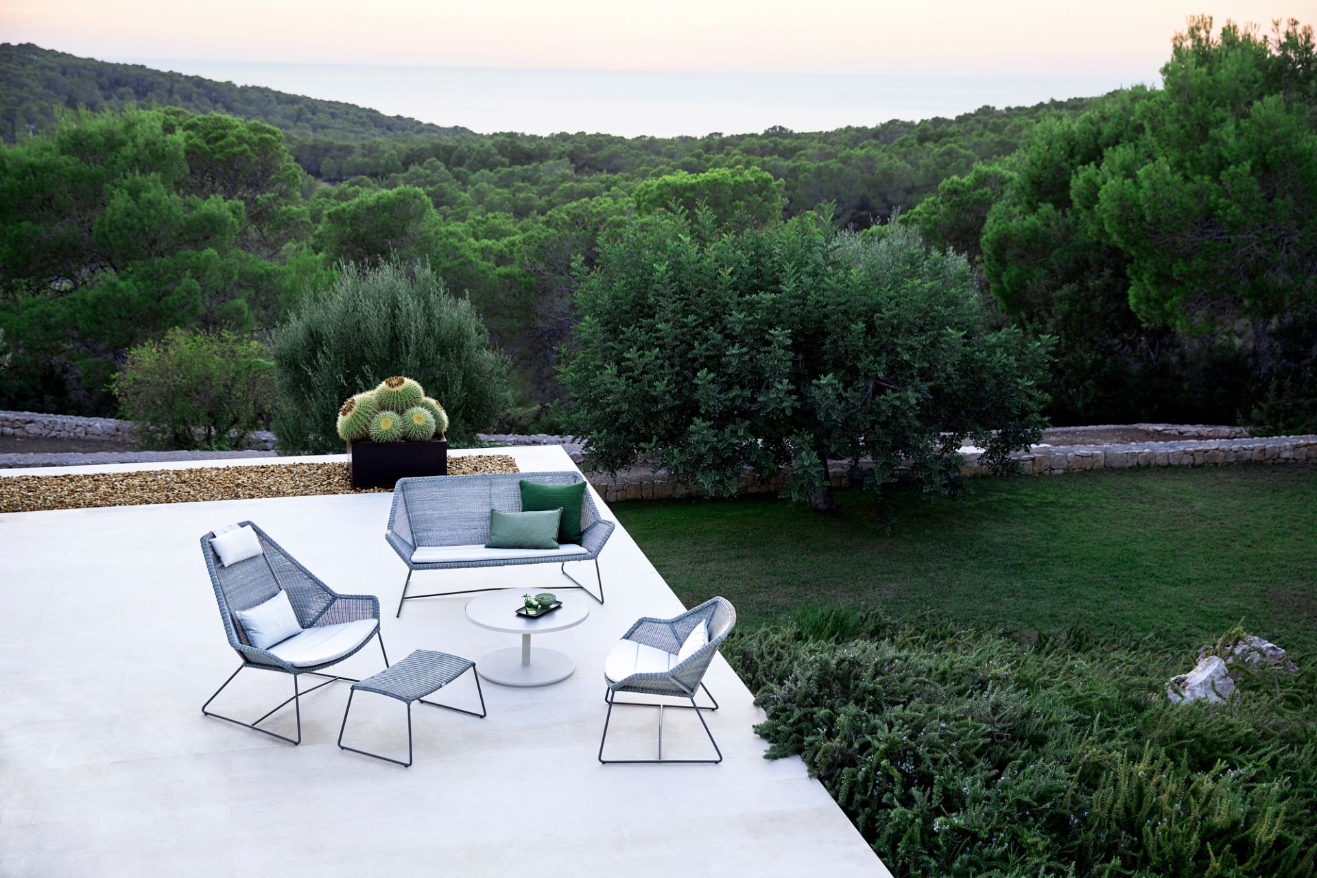 Graue Gartenmöbel-Loungegruppe mit Sofa, Sesseln und Tisch auf Terrasse mit Blick auf grüne Landschaft.