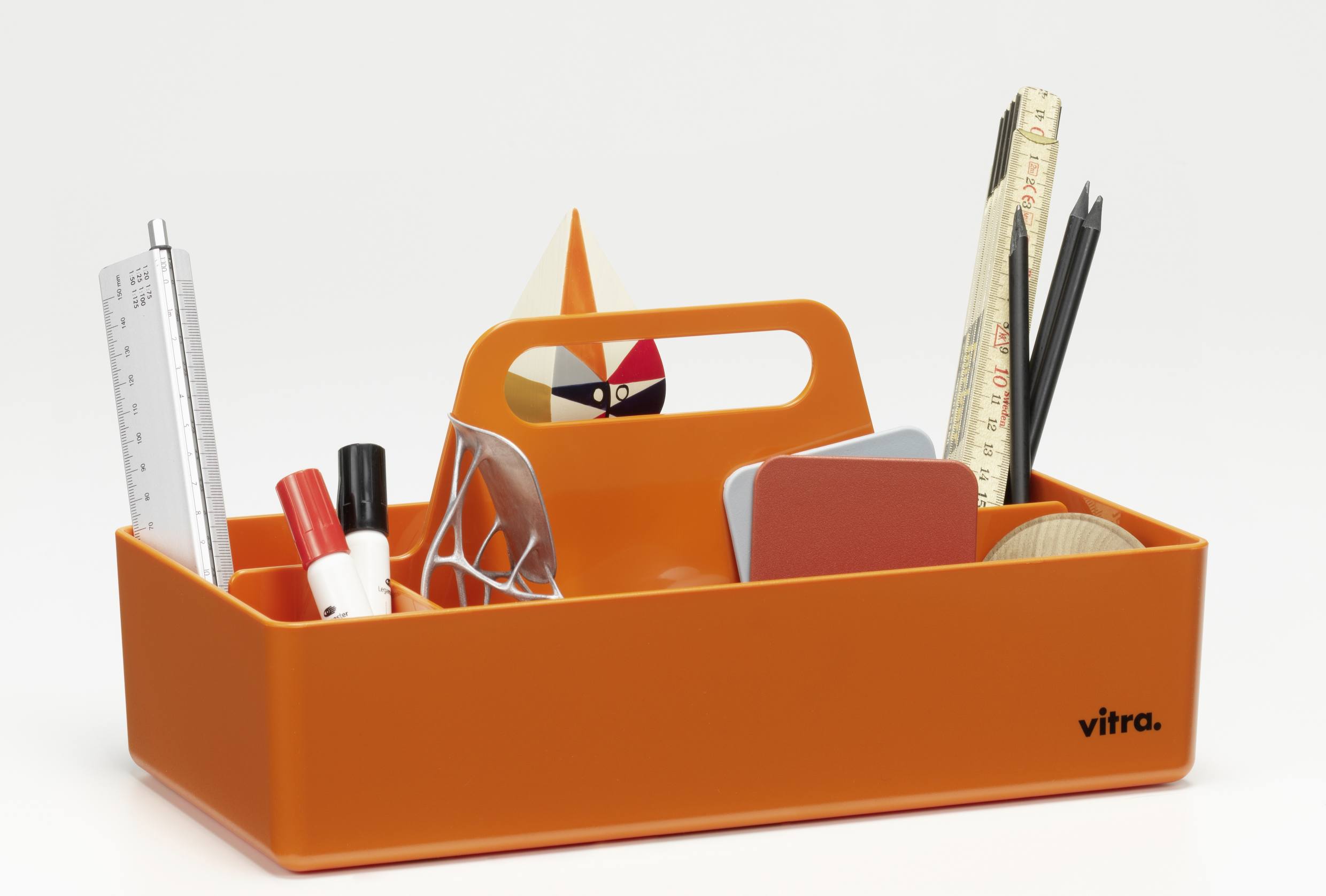 Vitra Toolbox RE, mandarinefarbene Aufbewahrungsbox mit Griff und diversen Büroartikeln wie Stiften, Lineal und Notizblöcken.