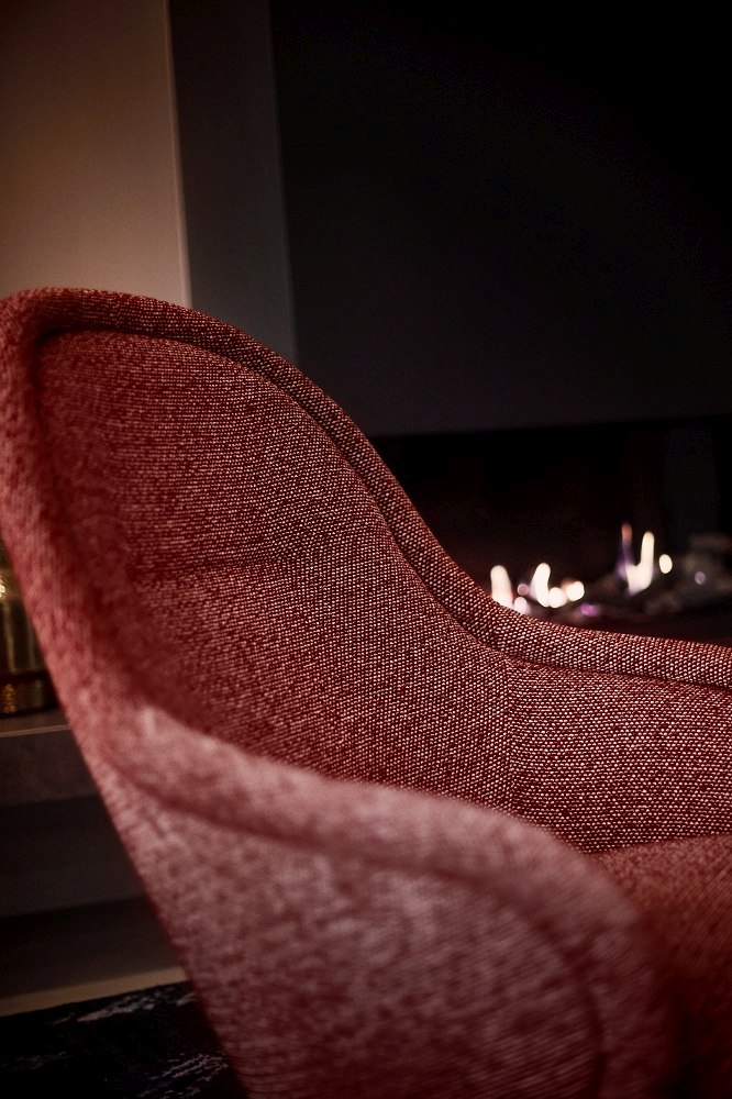 Detailaufnahme des roten Ona Lounge Sessels von Freifrau Manufaktur vor Kaminfeuer. Hochwertiger Design Sessel.
