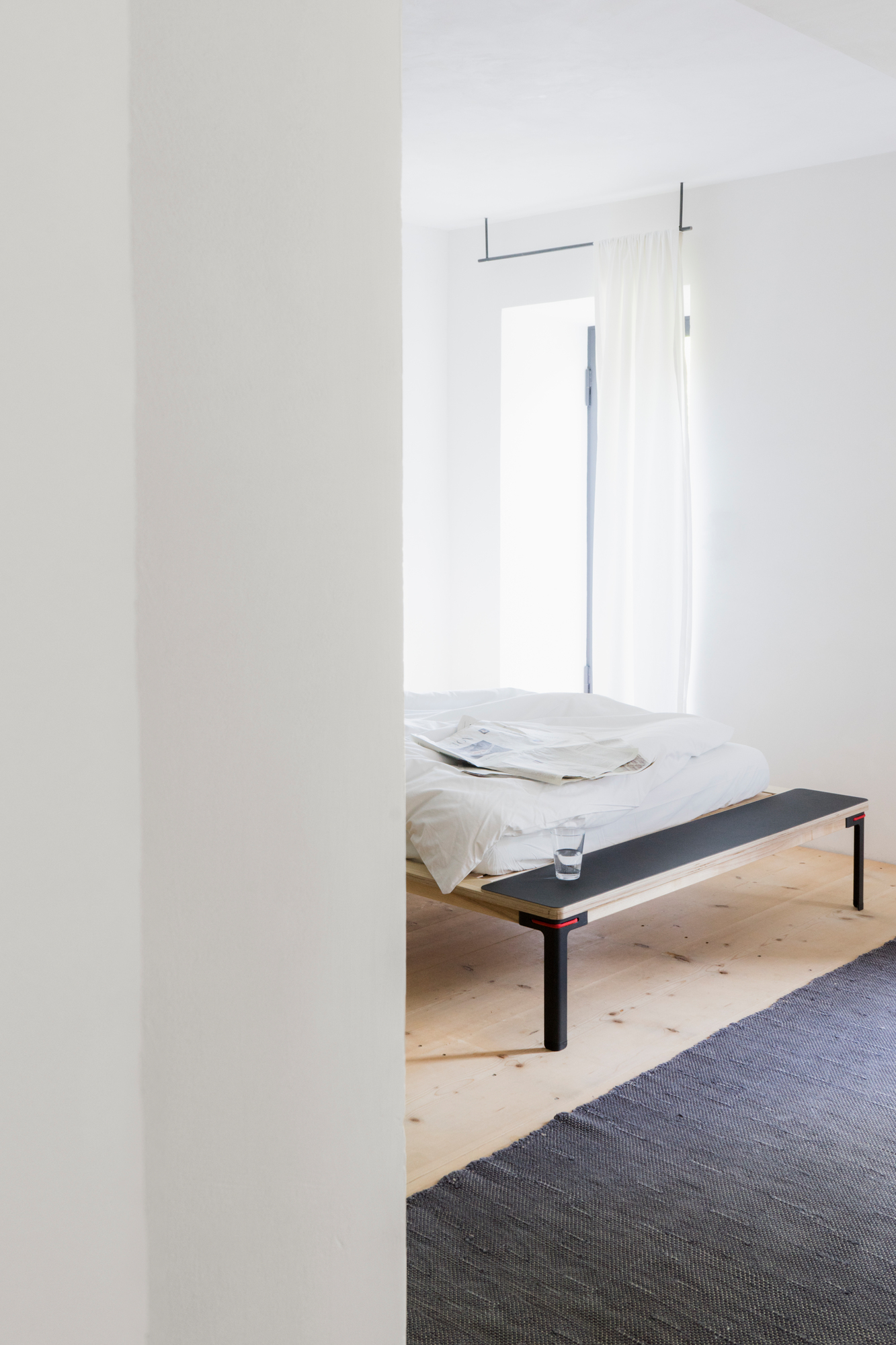 Rotes Seiltänzer Bett 160x200 von Nils Holger Moormann im minimalistischen Schlafzimmer mit Teppich.
