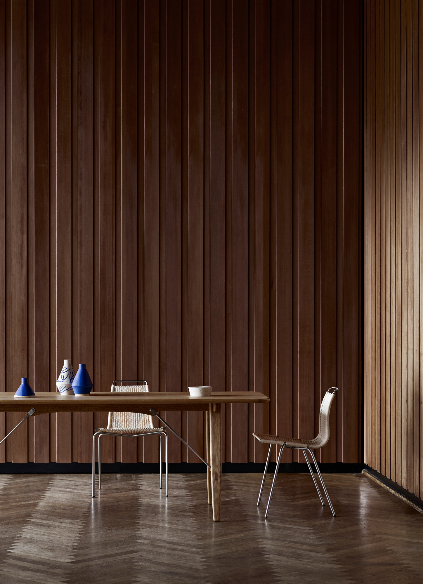 Hunting Table von Carl Hansen & Søn, geölt, mit Stühlen und Dekoration vor Holzpaneelen.