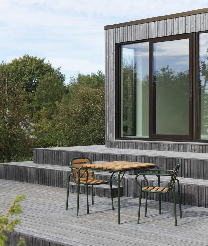 Normann Copenhagen Vig Armchair Armlehnstuhl Outdoor mit Holztisch auf einer Holzterrasse vor einem modernen Haus.