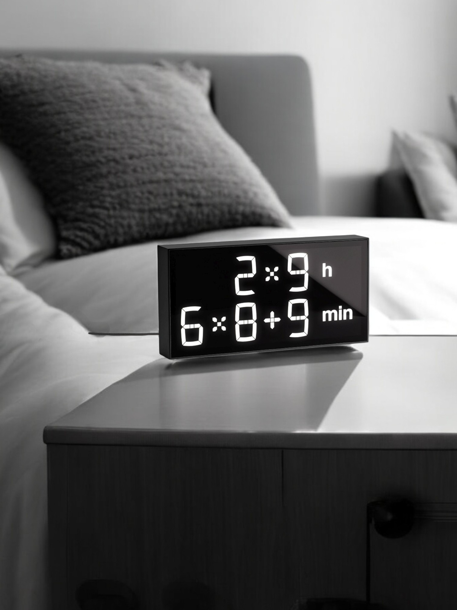 Schwarzer LED-Wecker mit mathematischer Formel zur Zeitanzeige auf einem Nachttisch im Schlafzimmer.