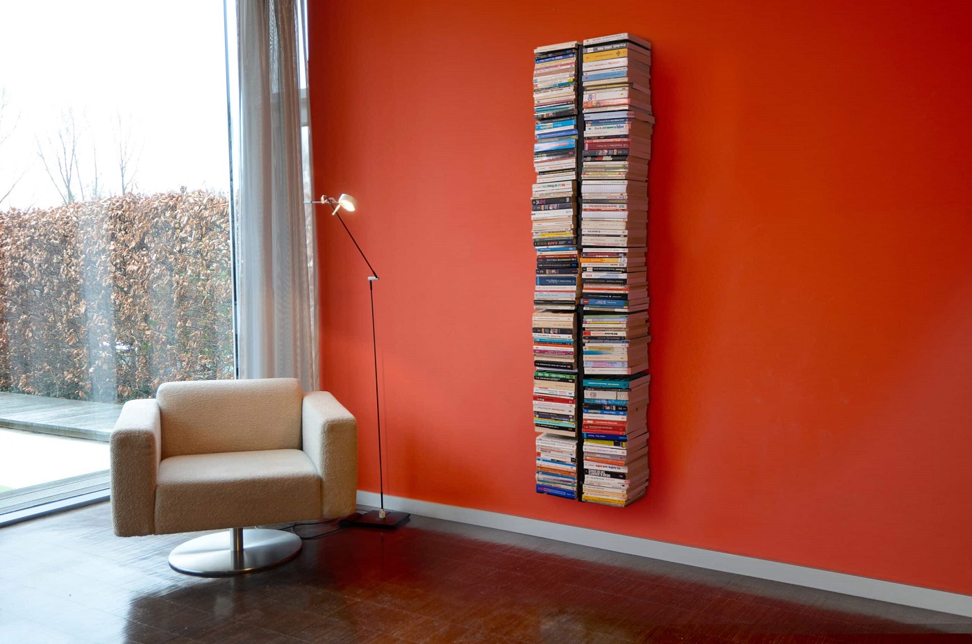 Booksbaum Wandregal: Hoher Bücherstapel als Design-Regal an roter Wand im Wohnzimmer.