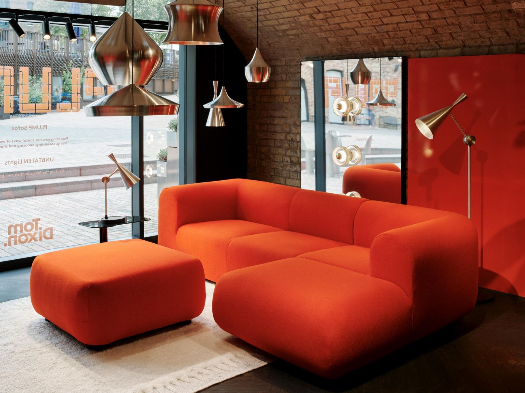 Innenarchitektur mit Tom Dixon Unbeaten Pendelleuchten, rotem Sofa und Stehlampe in modernem Ausstellungsraum.