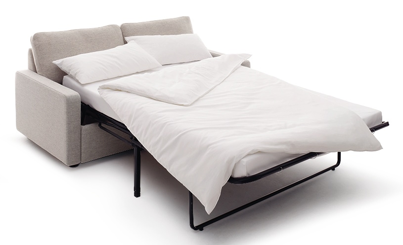 Conseta Schlafsofa Cor in Beige, ausgeklappt mit weißer Bettwäsche und Kissen, für komfortables Schlafen.