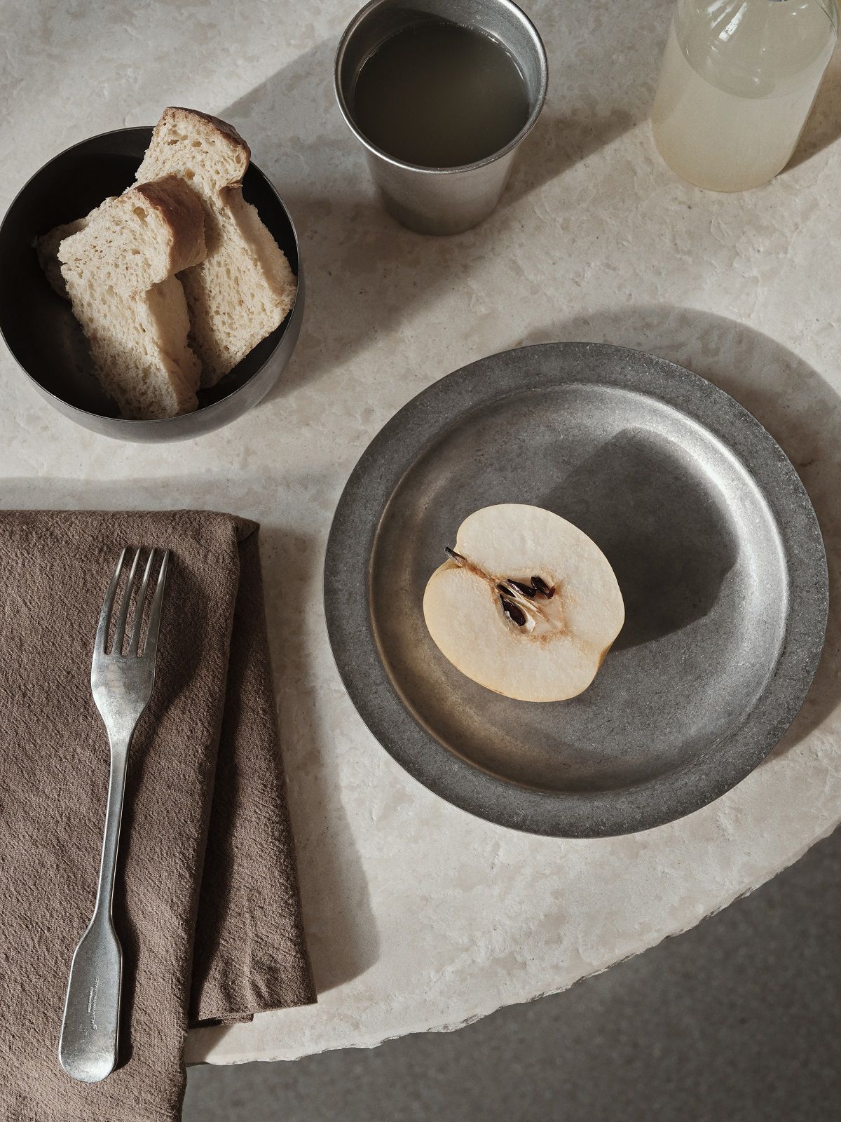 Ferm Living Tumbled Plate Campingteller mit Birnenhälfte, Brot, Getränken, Gabel und Serviette auf Tisch.