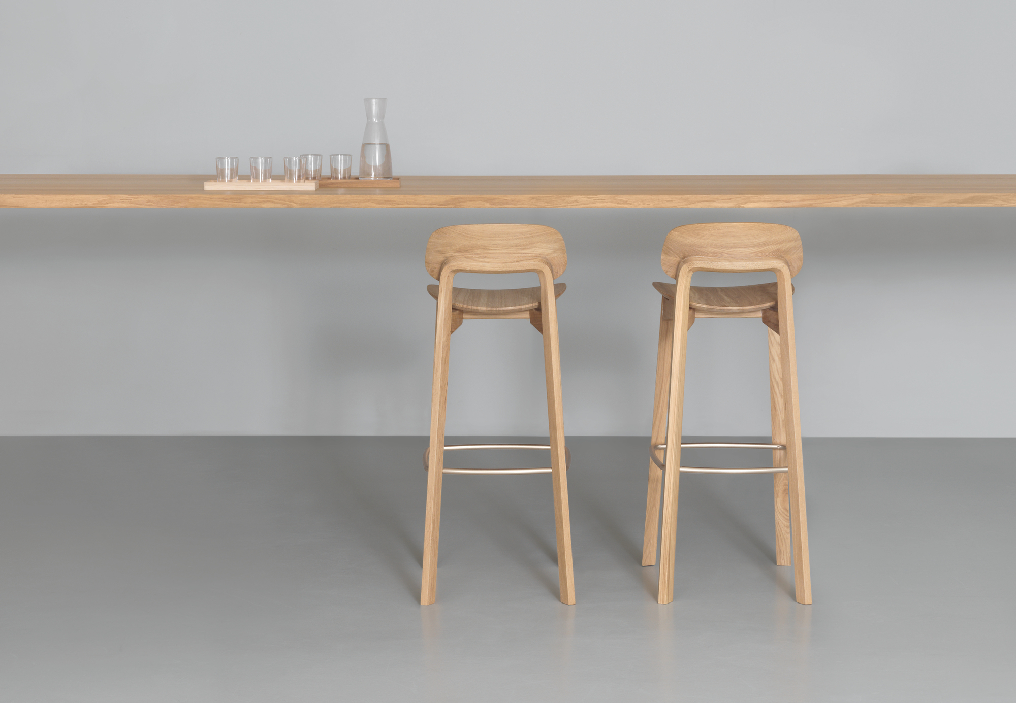 Zwei Nonoto Barhocker aus amerikanischem Nussbaum mit 80 cm Sitzhöhe vor einer Bartheke.