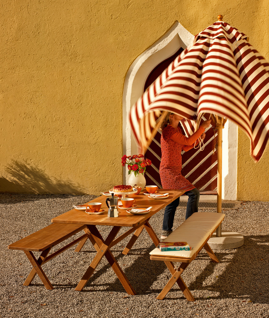 Weishäupl Cross Bank klappbar aus Holz mit Rückenlehne und passendem Gartentisch im Außenbereich.