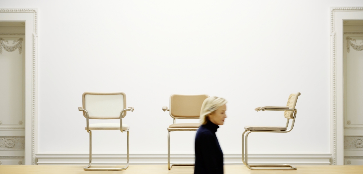 Drei JS. Thonet Freischwinger S 64 V Stühle in verschiedenen Ausführungen vor weißer Wand.