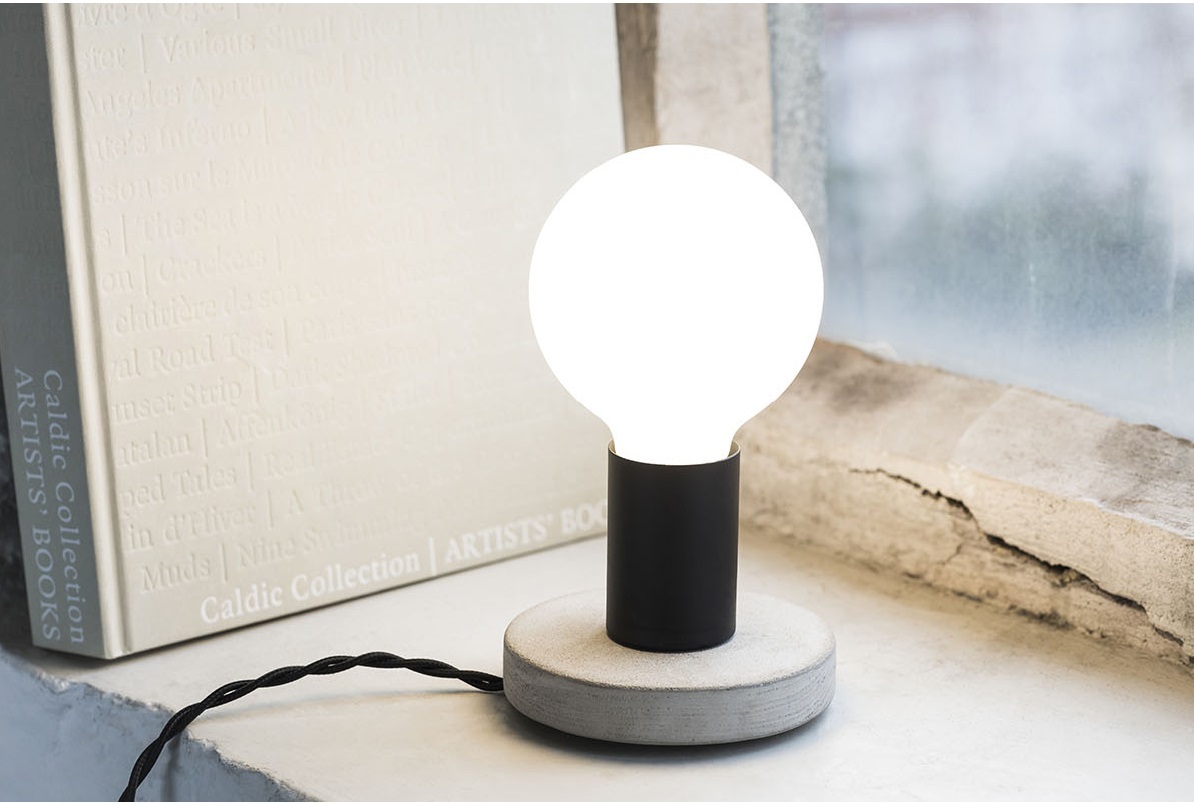 Essentials KVG Tischleuchte von Serax: Nahaufnahme der Lampe mit Betonfuß und Glühbirne.