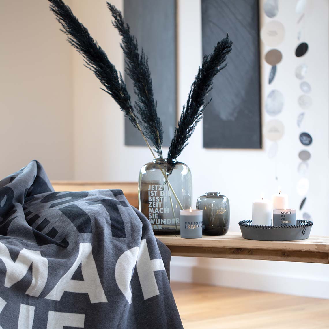 Dekorative Living "Beste Zeit" Glasvase mit Pampasgras, Kerzen und Decke auf einer Holzbank.