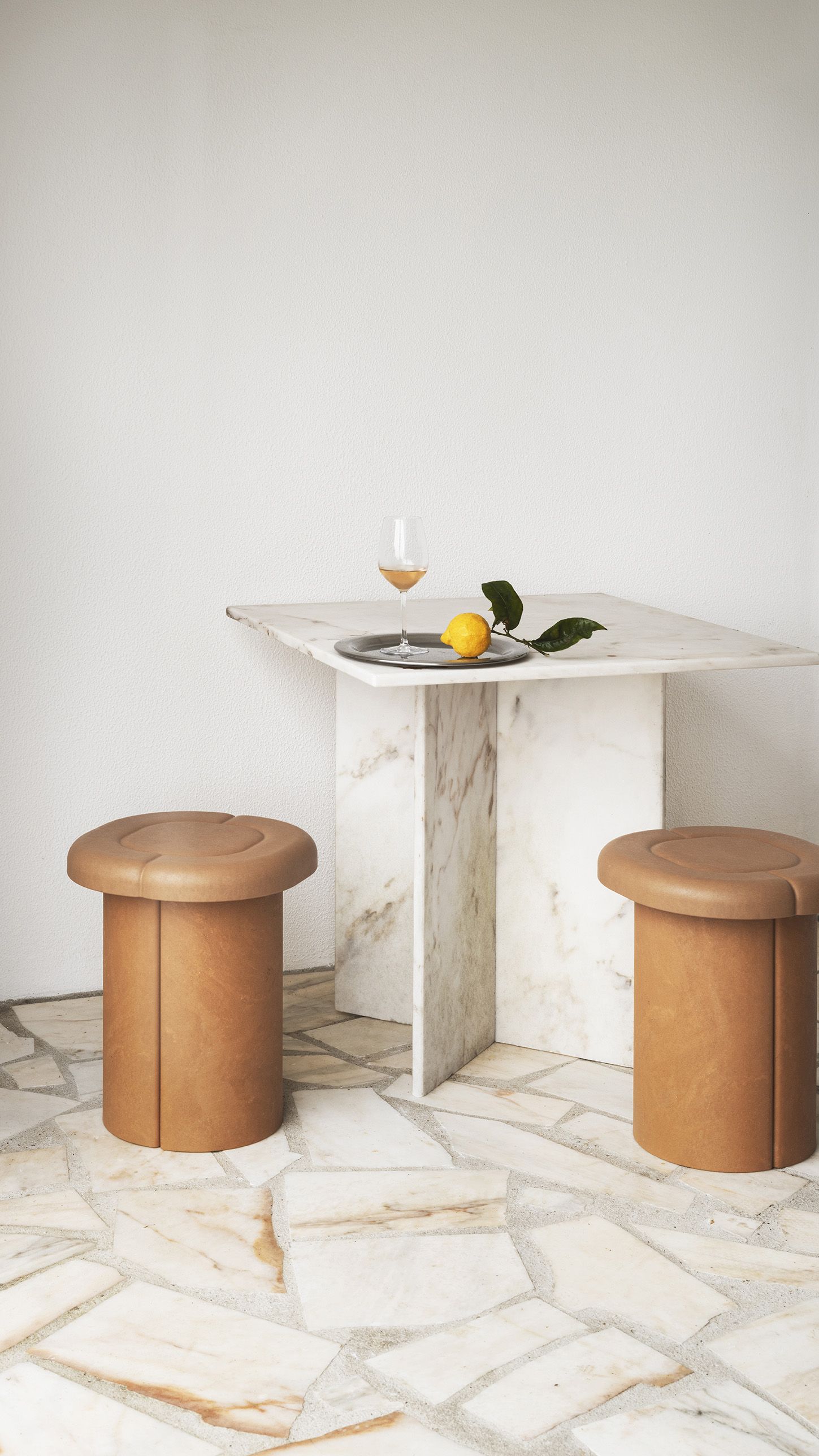 Zwei Alder Stool Hocker von Mater neben einem Marmortisch mit Zitrone und Getränk.