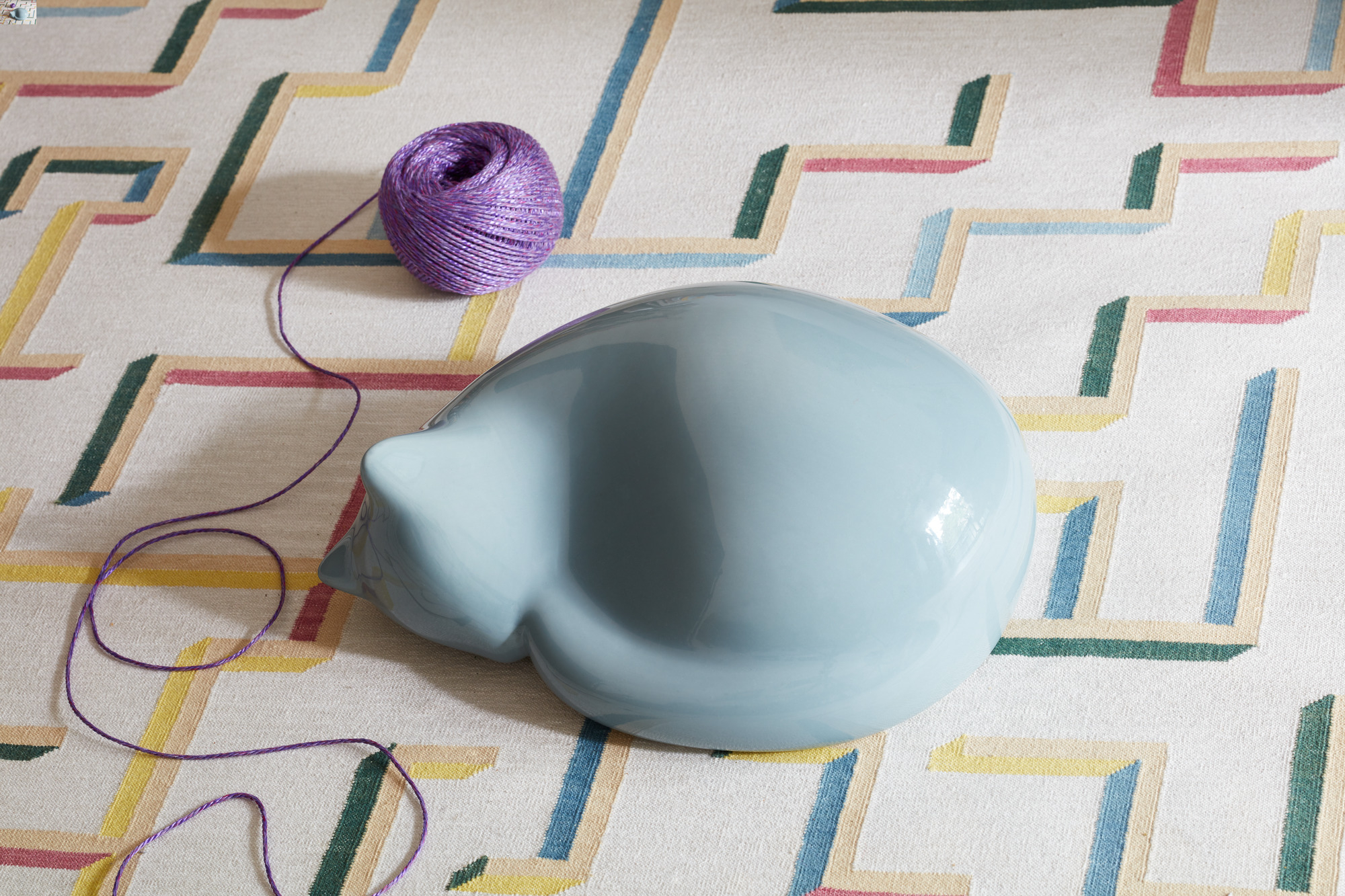 Hellblaue Vitra Katze Figur, schlafend auf einem Teppich mit lila Wollknäuel. Dekorative Katzenfigur.