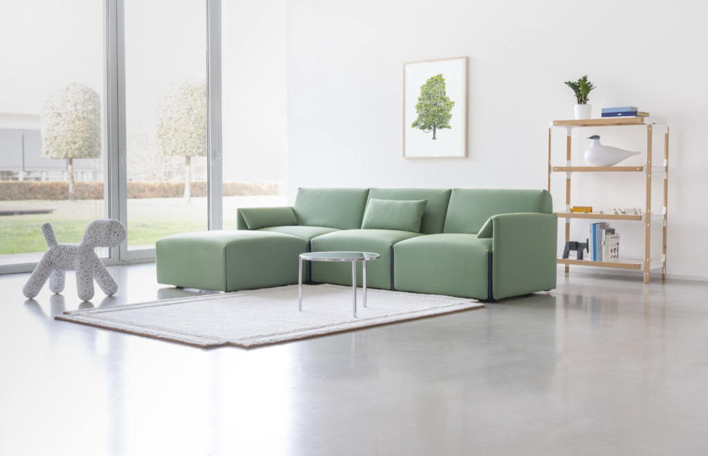 Helles Wohnzimmer mit grünem Costume Modulsofa, Teppich und Regal. Modernes Sofa für Wohnraumgestaltung.