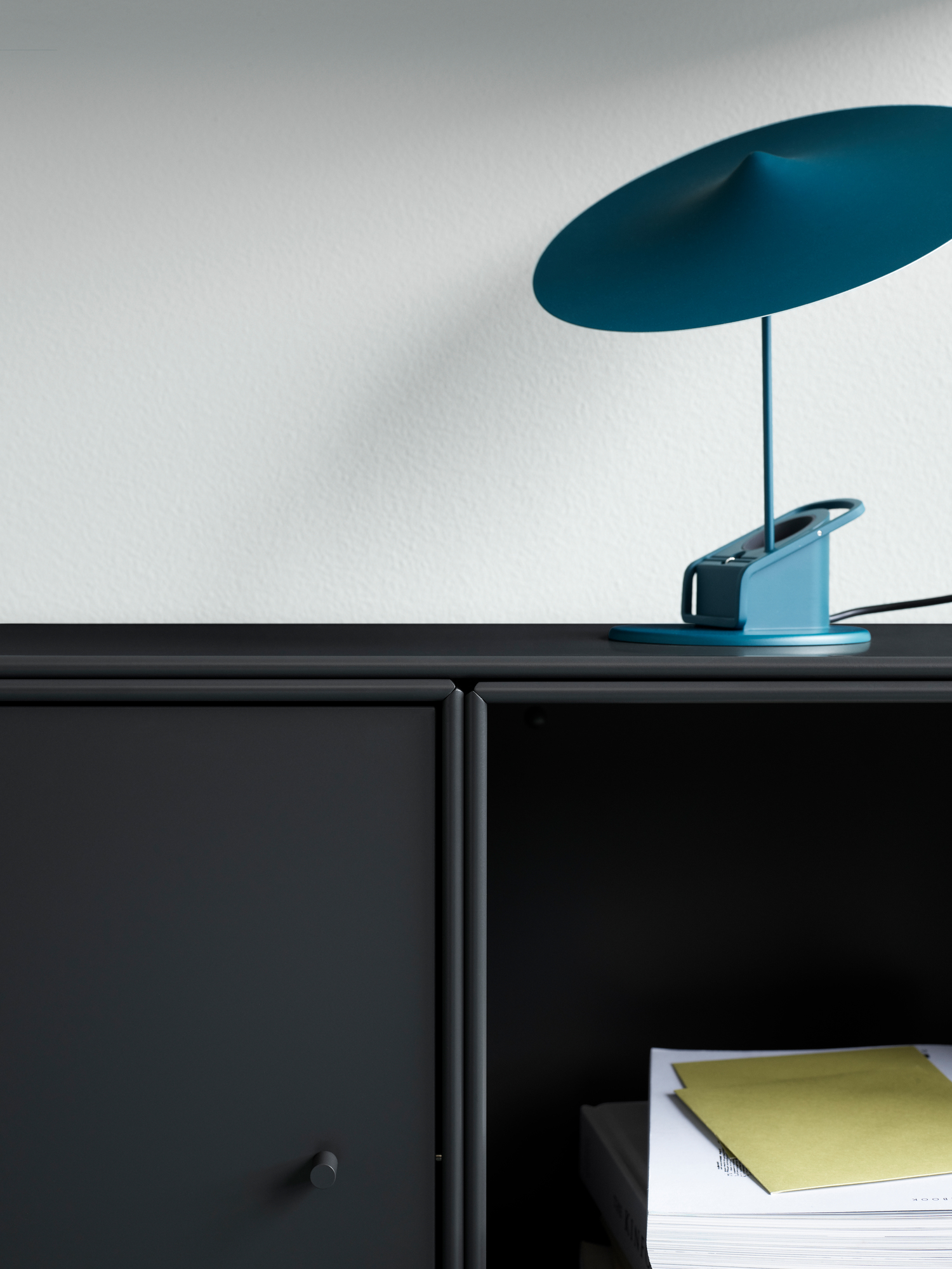 Nahaufnahme eines schwarzen Schranks mit Montana Abdeckplatte und blauer Lampe.