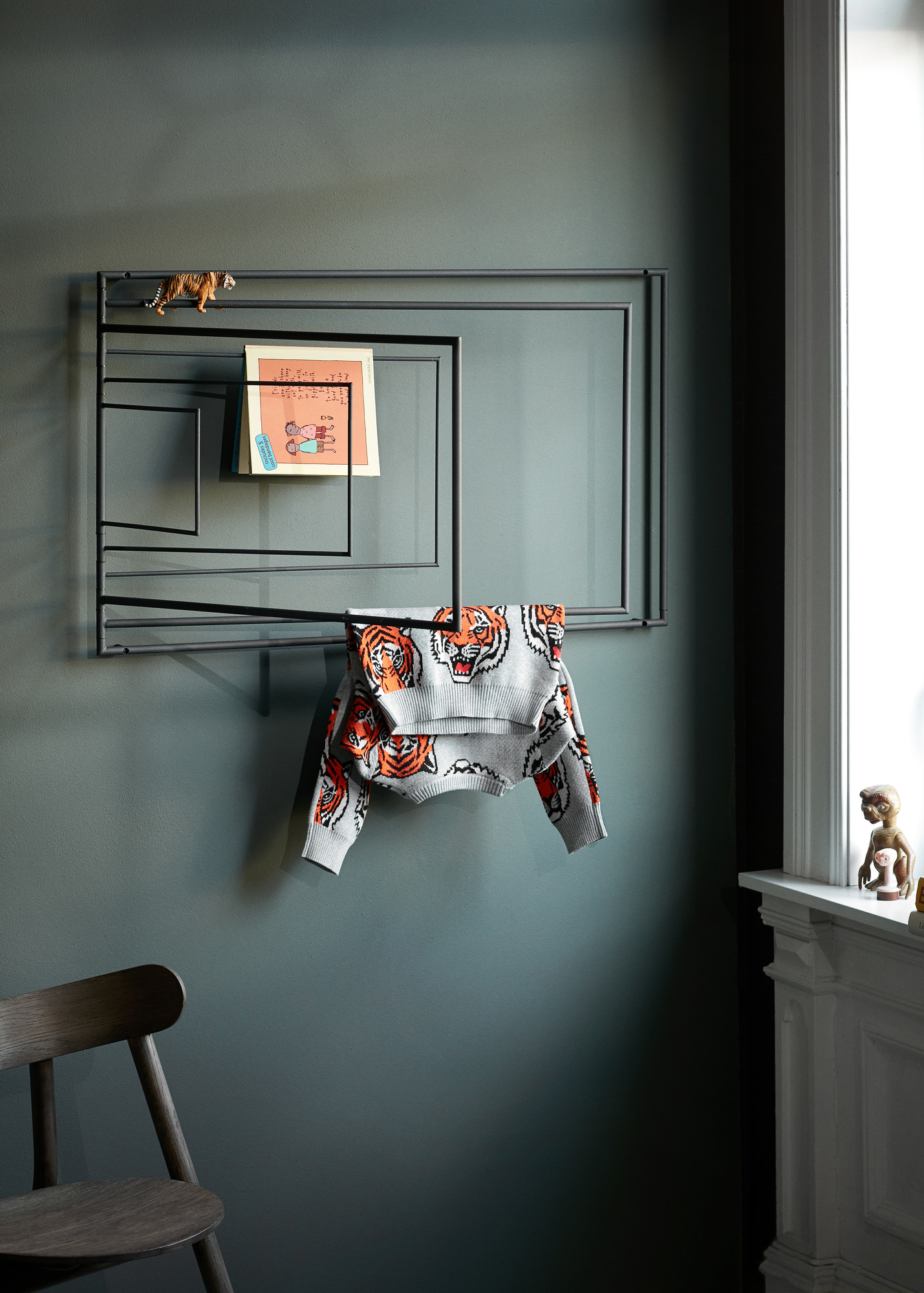 Frame Wandgarderobe: Moderne Wandgarderobe aus Metall mit Pullover, Notiz und Tigerfigur an grauer Wand.