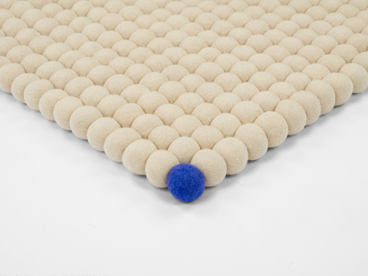 Beiger Filzteppich "Big One" (200x300 cm) aus Filzkugeln mit einer blauen Kugel.