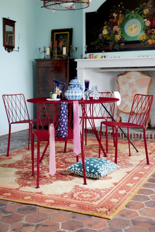 Rote Kintbury Stühle von Fermob um einen runden Tisch auf einem gemusterten Teppich. Outdoor-Möbel für Garten und Terrasse.