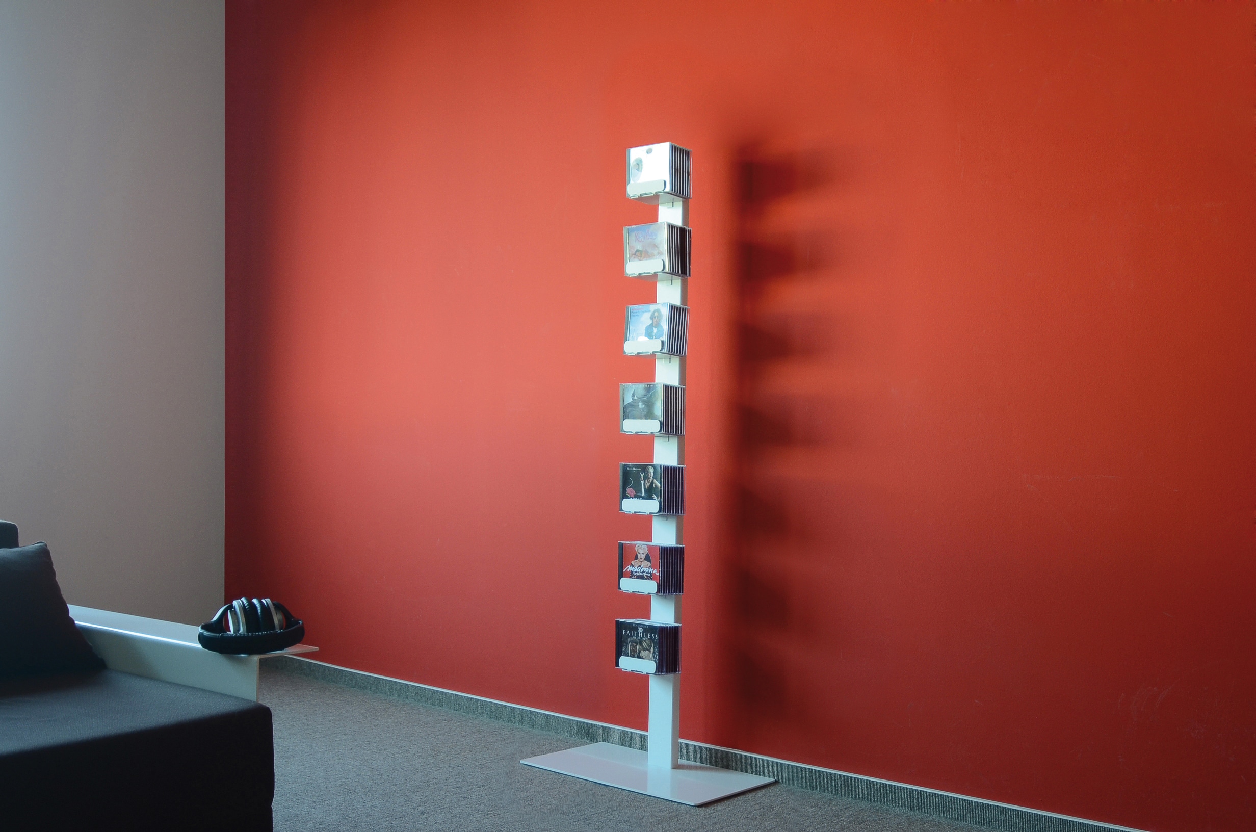 Weißes CD-Regal "CD-Baum" mit CDs vor roter Wand. Einzeln stehendes Standregal für CDs.